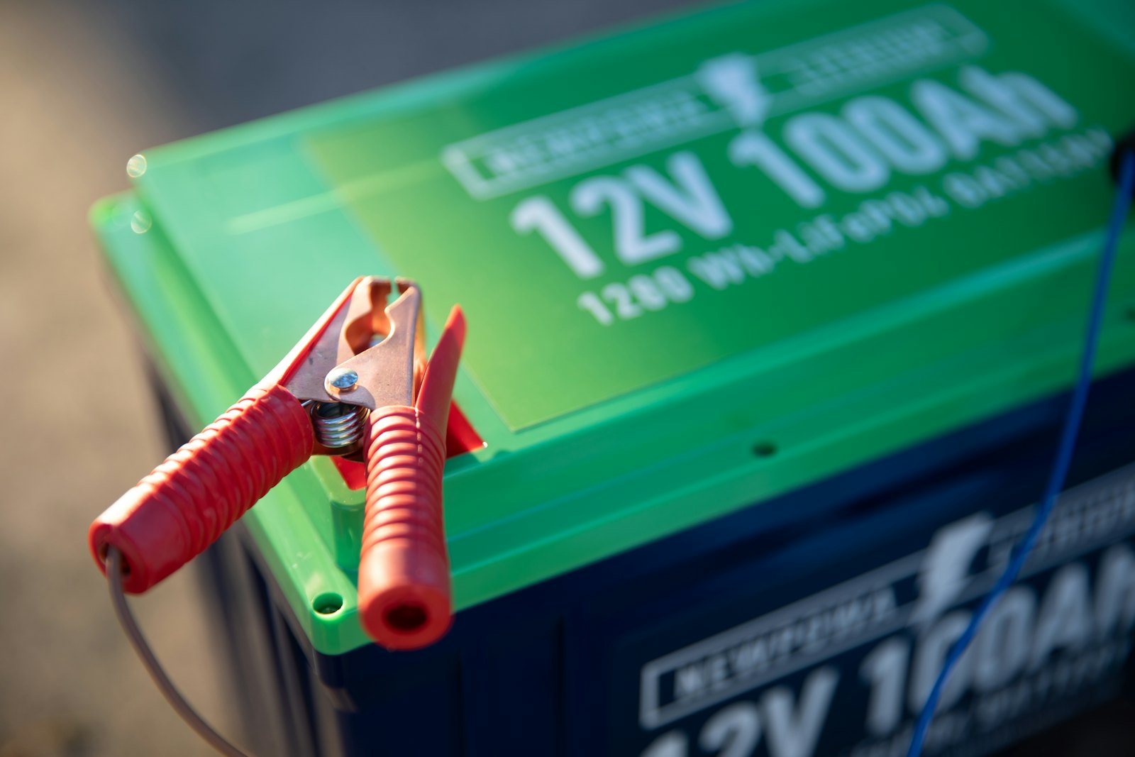 A red battery clamp connected to a 12V battery terminal